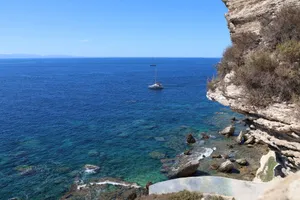 A serene view of a sailboat on the blue Mediterranean Sea near rocky cliffs. jigsaw puzzle