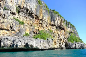 Majestic rocky cliff face beside a tranquil ocean under a bright blue sky. jigsaw puzzle
