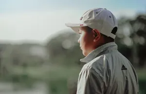 A boy wearing a white cap and jacket looks thoughtfully into the distance outdoors. jigsaw puzzle