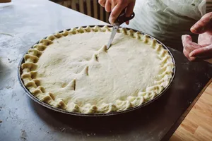 Hands skillfully trimming homemade pie crust with scissors in a kitchen setting. jigsaw puzzle