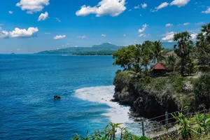 Stunning coastal view of Bali with a cliffside villa and lush palm trees under a clear blue sky. jigsaw puzzle