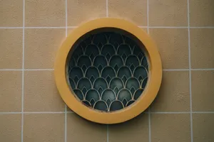 Circular window with decorative grille set in a yellow tiled wall, showcasing geometric patterns. jigsaw puzzle