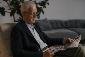 Elderly man in a black suit reads a newspaper indoors, reflecting a peaceful lifestyle. jigsaw puzzle
