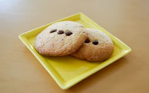 Two freshly baked chocolate chip cookies served on a yellow plate. jigsaw puzzle