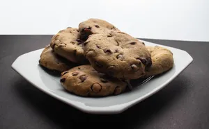 Sumptuous chocolate chip cookies stacked on a white plate, ready to enjoy. jigsaw puzzle