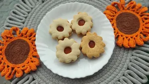 Four flower-shaped jam cookies on a white plate, surrounded by colorful crochet mats. jigsaw puzzle