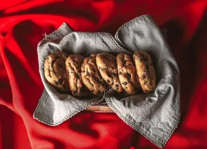 A batch of delicious chocolate chip cookies resting on a cloth with a vibrant red background. jigsaw puzzle
