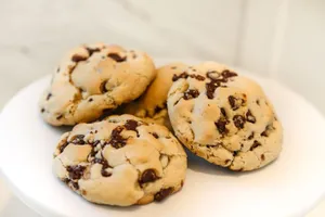 Close-up of freshly baked chocolate chip cookies on a white plate, showcasing gooey chocolate chunks. jigsaw puzzle
