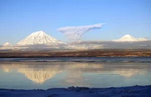 A serene view of snow-capped volcanoes reflecting in a tranquil lake at dawn. jigsaw puzzle