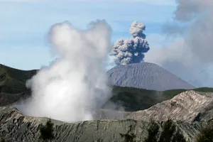 A dramatic aerial view of an erupting volcano with thick smoke plumes and rugged landscape. jigsaw puzzle