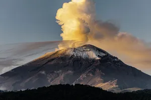 A majestic volcano erupts at sunset, emitting smoke and ash against a breathtaking landscape. jigsaw puzzle