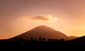 Silhouette of a volcano in Lanzarote at sunset, with a warm orange sky and clouds. jigsaw puzzle