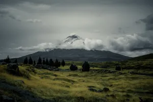Scenic view of a snowcapped volcano amidst a cloudy sky and expansive field. jigsaw puzzle