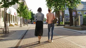 Two women enjoy a sunny walk down a lively urban street lined with buildings and trees. jigsaw puzzle