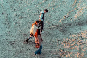Aerial shot of three people walking on a sandy beach during daytime, enjoying outdoor leisure. jigsaw puzzle