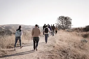 A group of adults hiking on a scenic, unpaved trail through dry grass and rolling hills on a sunny day. jigsaw puzzle