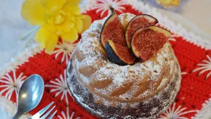 A freshly baked bundt cake topped with figs and dusted with powdered sugar, served on a vibrant red cloth with a flower for decoration. jigsaw puzzle