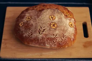 Close-up of artisan bread with intricate floral design on wooden board, ideal for bakery promotions. jigsaw puzzle