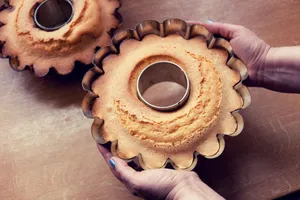 A freshly baked cake in a fluted mold held in hands over a kitchen table. jigsaw puzzle