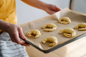 Person holding a baking sheet with raw croissants on parchment paper. jigsaw puzzle