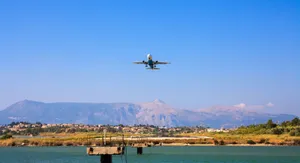 A plane flying over Corfu, Greece with mountains and water below, capturing a vibrant day scene. jigsaw puzzle