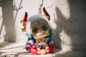 A vibrant anime-inspired figurine with horns sitting against a sunlit wall casting shadows. jigsaw puzzle
