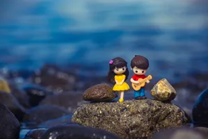 Adorable clay figures of a couple with a guitar on a rocky shore, set against a serene body of water. jigsaw puzzle