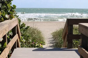 Wooden boardwalk leading to a sandy beach with waves in the background. jigsaw puzzle