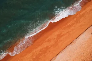 Explore the striking contrast of turquoise waves meeting vibrant orange sands from an aerial perspective. jigsaw puzzle