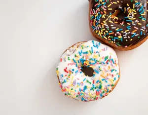 Two donuts with colorful sprinkles on a white surface, one with chocolate glaze, the other with vanilla. jigsaw puzzle