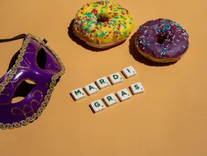 Festive Mardi Gras scene with colorful donuts, a purple mask, and Scrabble tiles on yellow background. jigsaw puzzle