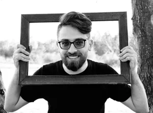 Smiling man with glasses holding a wooden frame outdoors in monochrome. jigsaw puzzle