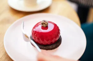 High angle of crop anonymous person eating delicious cake covered with red mirror glaze and served on white plate during coffee break in cafe jigsaw puzzle