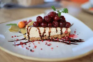 Close-up of a delectable cherry-topped cheesecake slice with chocolate drizzle on a ceramic plate. jigsaw puzzle