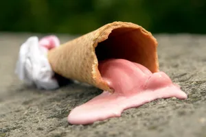 A melting strawberry ice cream cone lies on a stone surface, highlighting summer's heat. jigsaw puzzle
