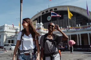 Two women walking and smiling outside in a city setting with a prominent train station in the background. jigsaw puzzle