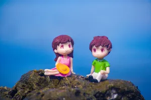 Charming toy figures of a boy and girl sitting on a mossy rock with a blue background, symbolizing youthful innocence. jigsaw puzzle