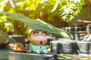 Charming cartoon figurine resting under leaf by seashell, surrounded by lush greenery and calming stone texture. jigsaw puzzle