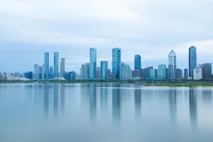 A serene view of modern skyscrapers reflecting on calm water under a cloudy sky. jigsaw puzzle