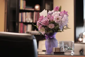 A beautiful bouquet of flowers in a purple vase adorns an office with bookshelves. jigsaw puzzle
