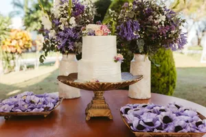 Chic white wedding cake adorned with soft pink and purple flowers, set in a vibrant outdoor arrangement. jigsaw puzzle