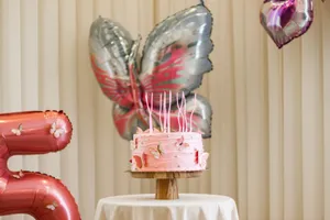 Pink birthday cake with butterfly decorations, surrounded by balloons indoors. jigsaw puzzle