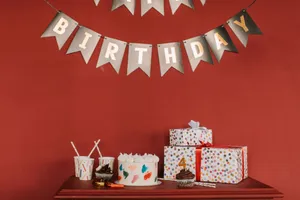 Festive birthday scene with cake, cupcakes, gifts, and decorations against red wall. jigsaw puzzle
