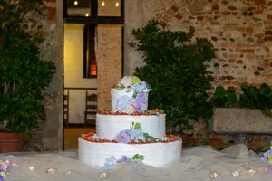 Three-tier wedding cake adorned with fresh flowers and strawberries, set in a rustic indoor venue. jigsaw puzzle