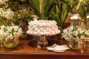 A beautifully decorated white cake surrounded by lush greenery and white floral arrangements on a wooden table. jigsaw puzzle