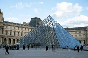 The iconic glass pyramid of the Louvre Museum in Paris with visitors on a clear day. jigsaw puzzle