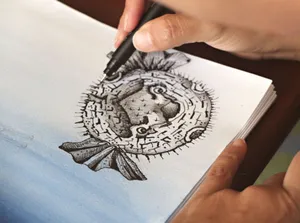 Close-up of a hand drawing a detailed pufferfish illustration in black ink on paper. jigsaw puzzle