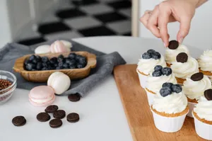 High angle of crop anonymous confectioner decorating delicious cupcakes with blueberries and chocolate cookies on table jigsaw puzzle