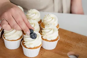 Close-up of hand adding blueberries to cupcakes with creamy frosting on a wooden table. jigsaw puzzle