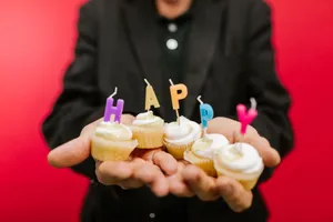 Colorful cupcakes with 'HAPPY' candles held in hands against a red background. jigsaw puzzle
